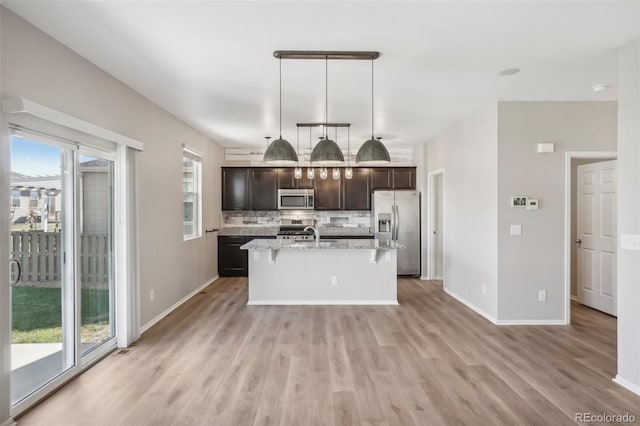 kitchen featuring tasteful backsplash, an island with sink, decorative light fixtures, dark brown cabinets, and appliances with stainless steel finishes