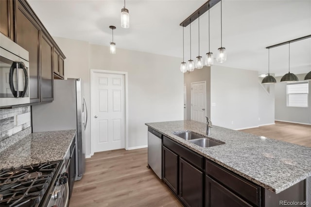 kitchen with sink, an island with sink, decorative light fixtures, dark brown cabinets, and stainless steel appliances