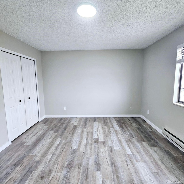 25 Castle Royal Dr, Pueblo, CO 81005 - unfurnished bedroom with wood finished floors, a textured ceiling, a baseboard heating unit, a closet, and baseboards