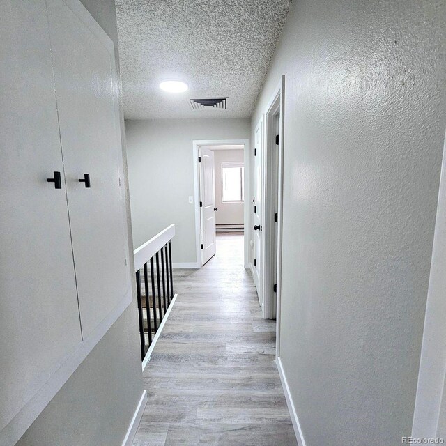25 Castle Royal Dr, Pueblo, CO 81005 - hall with baseboards, light wood finished floors, a textured wall, a textured ceiling, and a baseboard radiator
