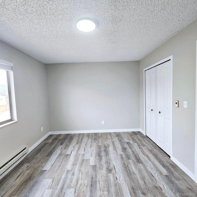 25 Castle Royal Dr, Pueblo, CO 81005 - unfurnished bedroom with a baseboard radiator, wood finished floors, a textured ceiling, a closet, and baseboards