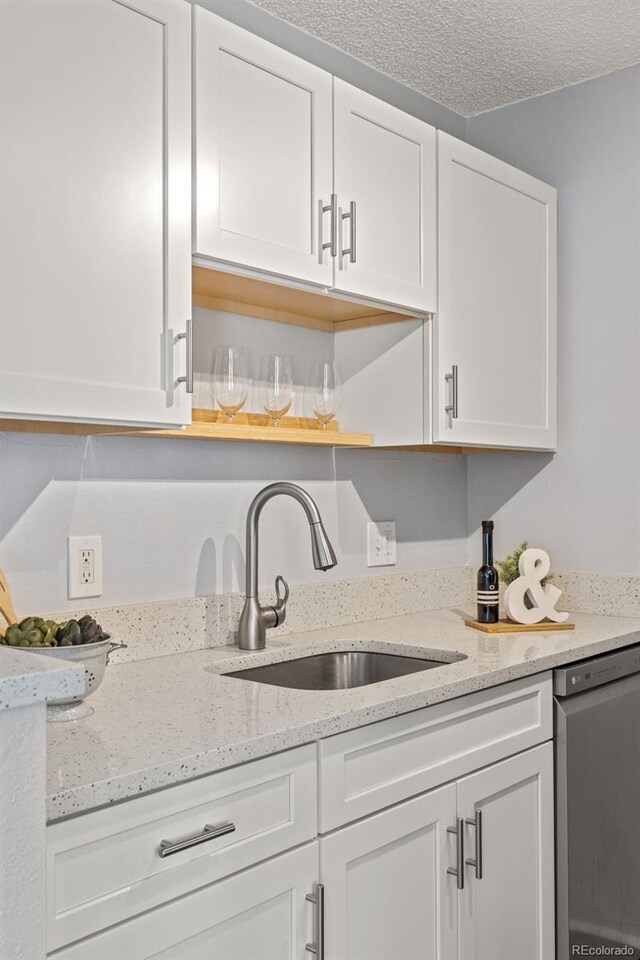 kitchen with light stone countertops, a textured ceiling, stainless steel dishwasher, white cabinetry, and a sink