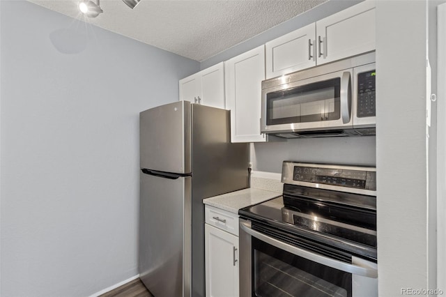 kitchen featuring stainless steel appliances, white cabinets, a textured ceiling, and baseboards