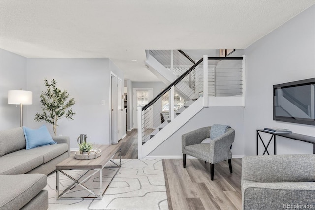 living room featuring a textured ceiling, stairs, baseboards, and wood finished floors