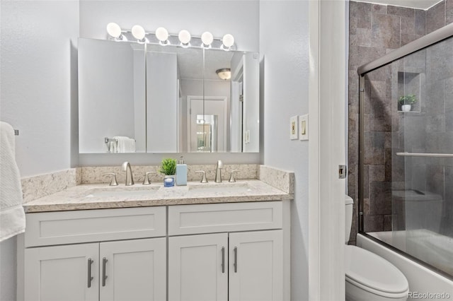 bathroom with double vanity, a sink, toilet, and bath / shower combo with glass door