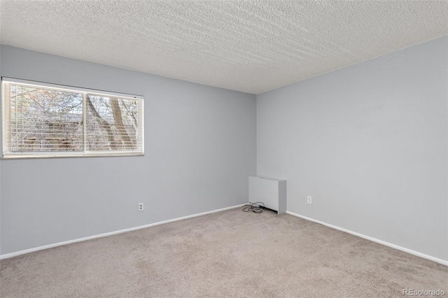 spare room with light carpet, a textured ceiling, and baseboards