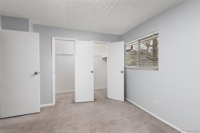 unfurnished bedroom with a spacious closet, baseboards, a textured ceiling, and light colored carpet