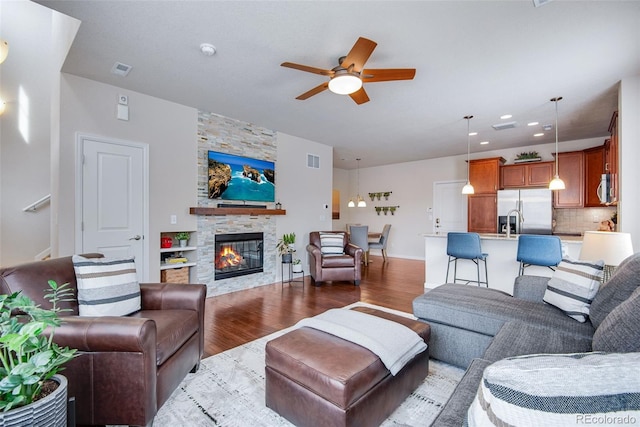 living room with a fireplace, dark wood-style flooring, a ceiling fan, and visible vents