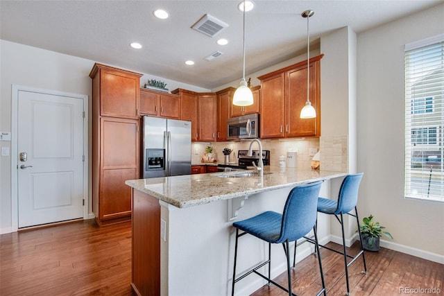 kitchen featuring a peninsula, brown cabinetry, visible vents, appliances with stainless steel finishes, and dark wood-style floors