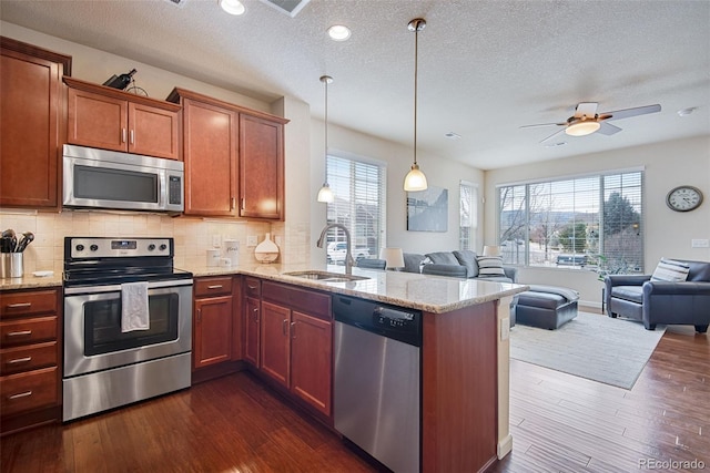 kitchen with a sink, a peninsula, stainless steel appliances, a textured ceiling, and open floor plan