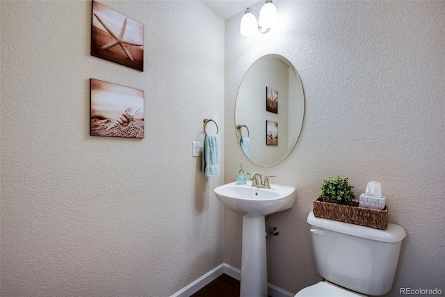 half bath with toilet, baseboards, and a sink