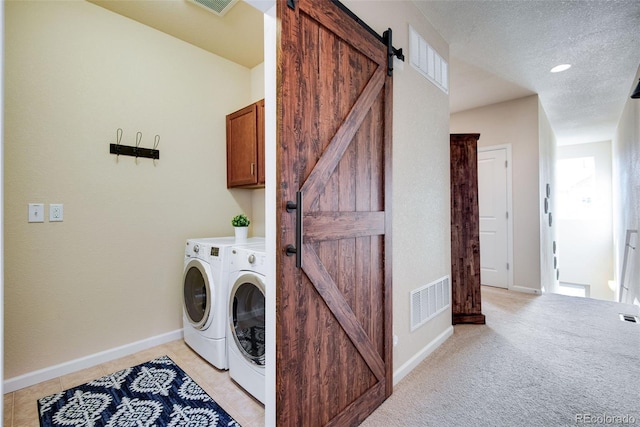 clothes washing area with washer and clothes dryer, a barn door, cabinet space, and visible vents