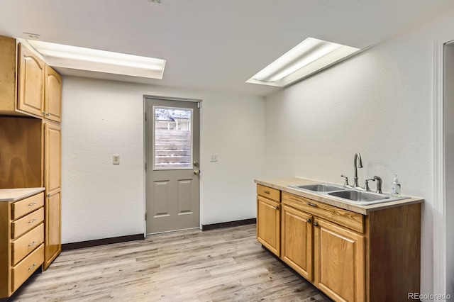 kitchen with baseboards, a sink, light countertops, light wood-type flooring, and a skylight