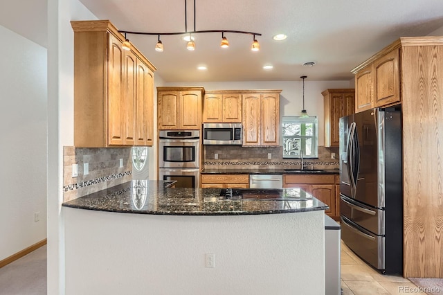 kitchen with a sink, a peninsula, stainless steel appliances, tasteful backsplash, and dark stone countertops