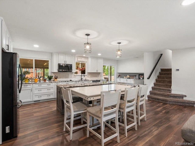 6166 S Dover St, Littleton, CO 80123 - kitchen featuring freestanding refrigerator, stainless steel microwave, white cabinets, dark wood-style flooring, and a kitchen breakfast bar