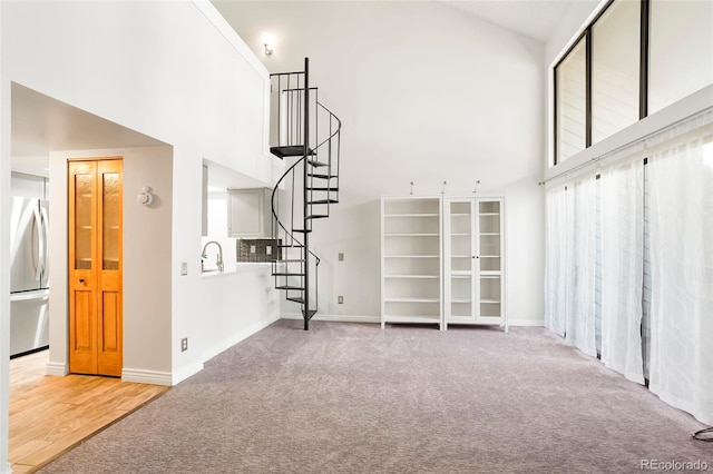 unfurnished living room with high vaulted ceiling, stairway, carpet flooring, and baseboards