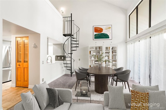 dining space featuring stairway, high vaulted ceiling, baseboards, and wood finished floors