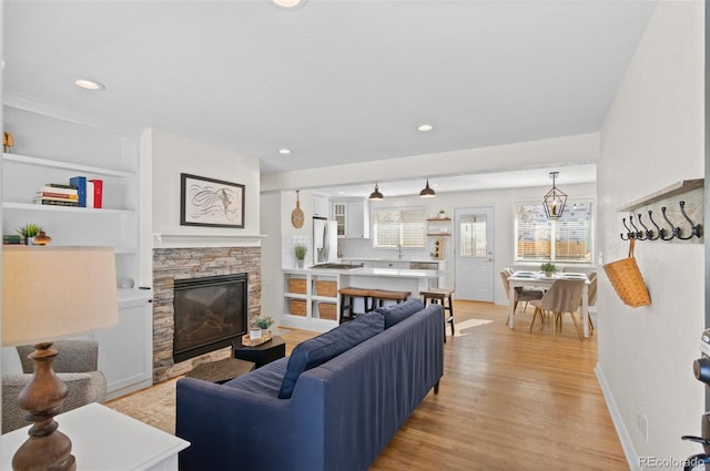 living room featuring a stone fireplace, light hardwood / wood-style flooring, and built in shelves