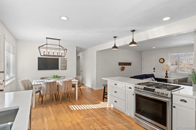 kitchen with stainless steel gas stove, hanging light fixtures, white cabinetry, and plenty of natural light