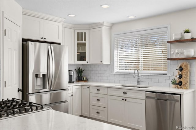 kitchen with stainless steel appliances, white cabinetry, sink, and backsplash