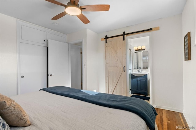 bedroom featuring hardwood / wood-style floors, sink, ceiling fan, a barn door, and ensuite bath