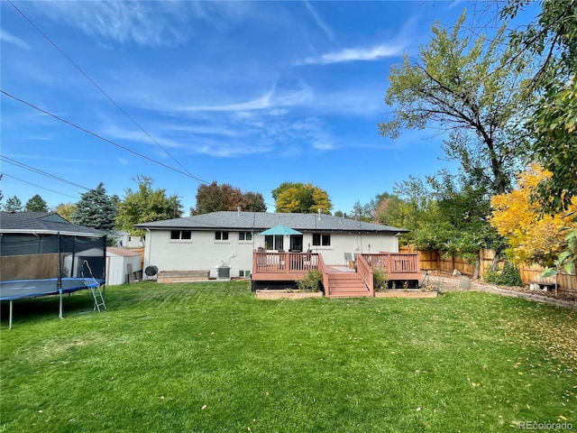 rear view of house with a wooden deck, a yard, a trampoline, and a storage unit