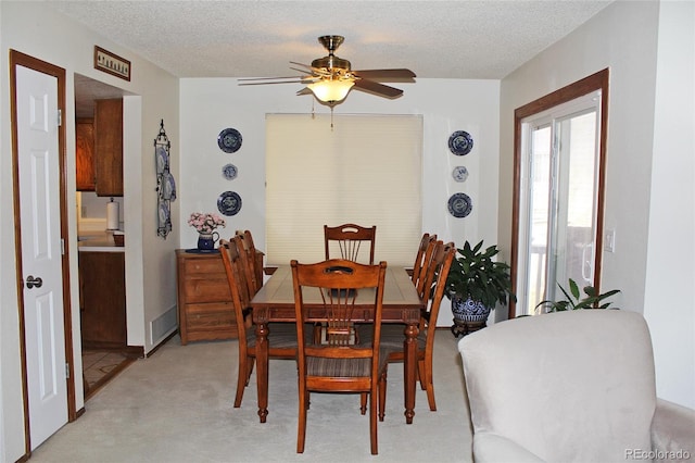 dining space with a textured ceiling, light colored carpet, and ceiling fan