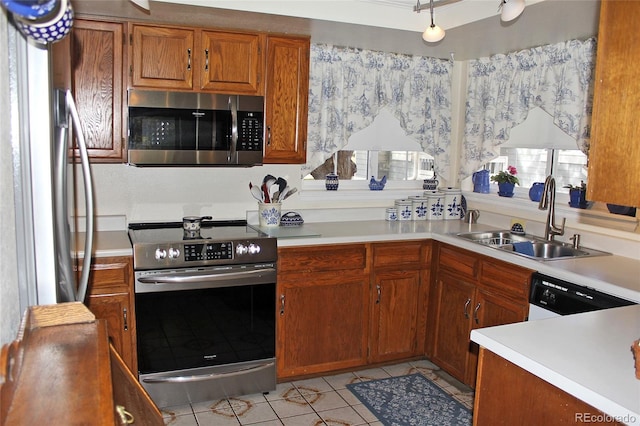 kitchen with stainless steel appliances, light tile patterned floors, a sink, brown cabinets, and light countertops