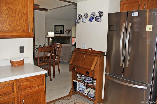 kitchen with freestanding refrigerator, brown cabinetry, a fireplace, light colored carpet, and light countertops