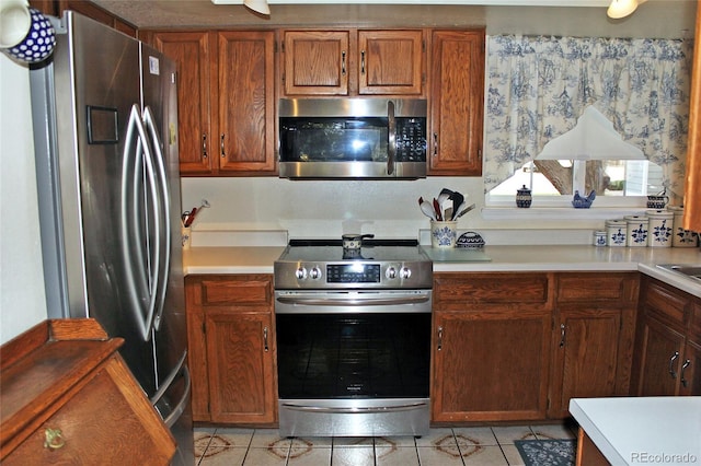kitchen with light tile patterned floors, light countertops, brown cabinetry, and appliances with stainless steel finishes