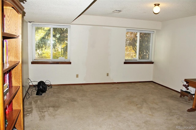 carpeted empty room featuring a textured ceiling, visible vents, and baseboards