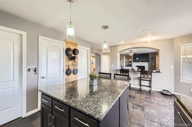 9990 Jasper St, Commerce City, CO 80022 - kitchen with arched walkways, baseboards, a fireplace, and dark cabinetry