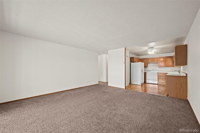 unfurnished living room featuring baseboards, light colored carpet, ceiling fan, a textured ceiling, and a sink