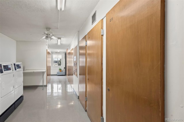 hall with a textured ceiling, separate washer and dryer, visible vents, and baseboards