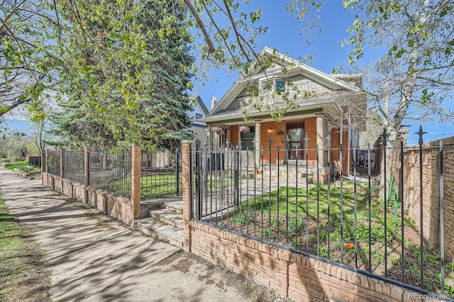 view of front of property featuring a porch, a fenced front yard, brick siding, and a gate