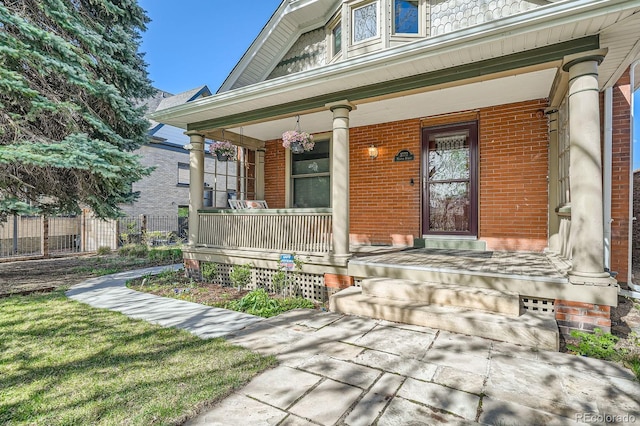 view of exterior entry featuring a porch, brick siding, and fence