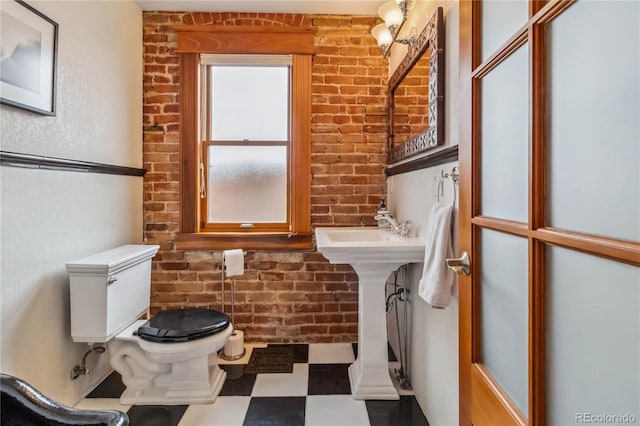 bathroom with tile patterned floors, toilet, and brick wall