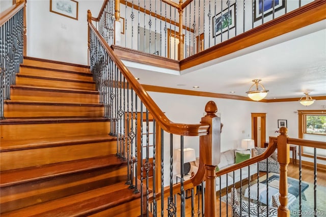 staircase featuring wood finished floors, crown molding, a high ceiling, and baseboards