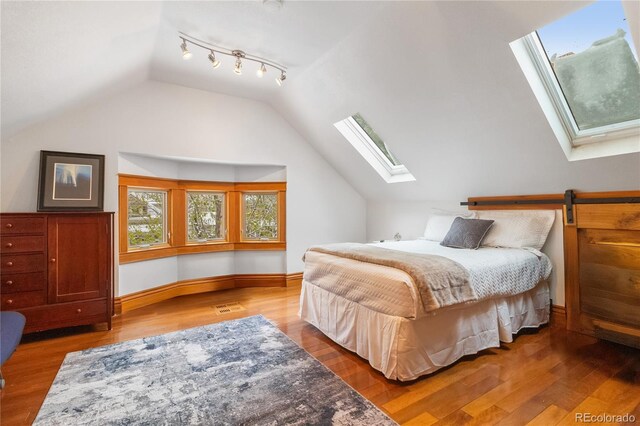 bedroom with a skylight, lofted ceiling, wood finished floors, and baseboards