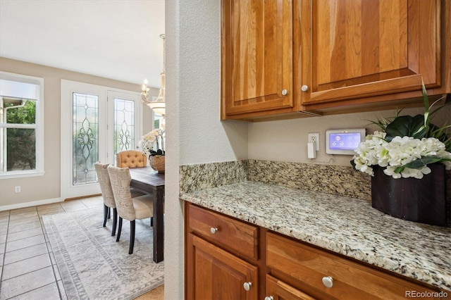 2601 Pemberly Ave, Highlands Ranch, CO 80126 - kitchen with brown cabinetry, light stone counters, baseboards, light tile patterned floors, and a chandelier