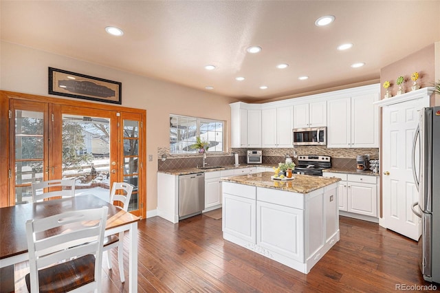 kitchen featuring stainless steel appliances, a center island, french doors, light stone counters, and white cabinets