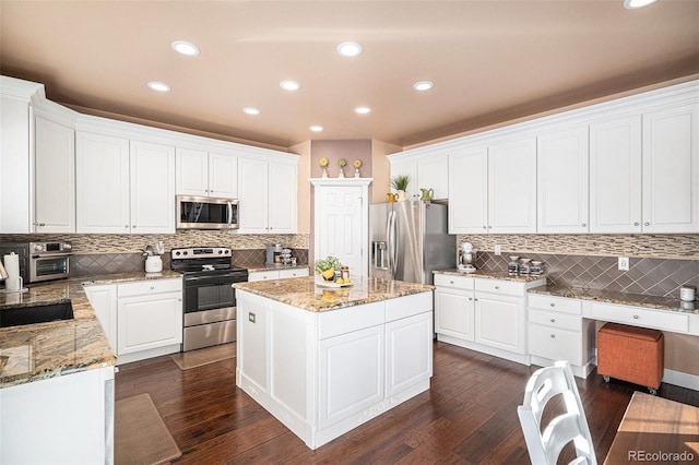 kitchen with appliances with stainless steel finishes, dark wood-type flooring, light stone counters, a kitchen island, and white cabinets