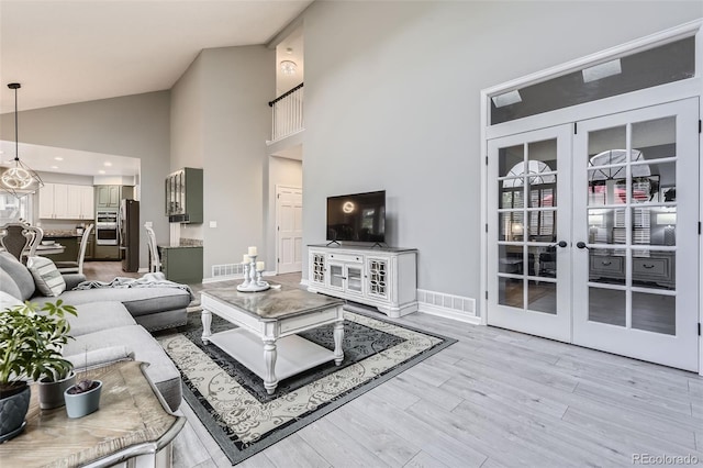 living room featuring high vaulted ceiling, french doors, light wood-style flooring, and baseboards