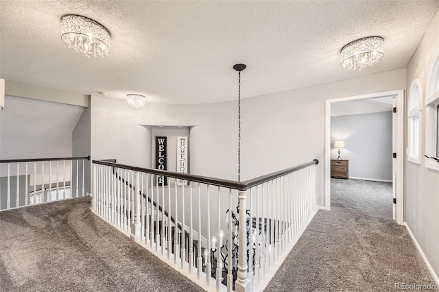 hall with a chandelier, carpet, a textured ceiling, an upstairs landing, and baseboards