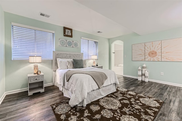bedroom with arched walkways, wood finished floors, baseboards, and ensuite bathroom