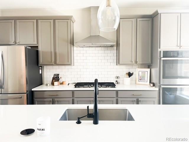 kitchen with stainless steel appliances, wall chimney exhaust hood, sink, gray cabinets, and backsplash