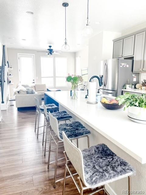 kitchen with pendant lighting, stainless steel fridge, gray cabinets, a kitchen breakfast bar, and hardwood / wood-style floors