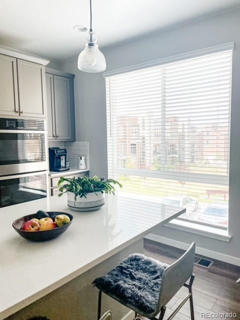 kitchen with tasteful backsplash, hardwood / wood-style flooring, stainless steel double oven, gray cabinets, and decorative light fixtures