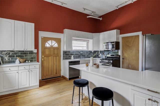 kitchen with appliances with stainless steel finishes, track lighting, a high ceiling, a breakfast bar, and decorative backsplash