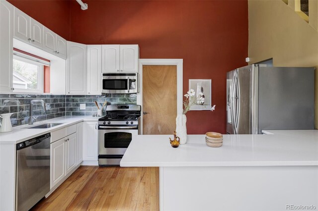 kitchen with stainless steel appliances, white cabinets, decorative backsplash, light countertops, and a high ceiling